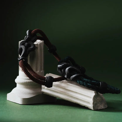 Blackened Black Mamba rope bracelet displayed on a green sculpture