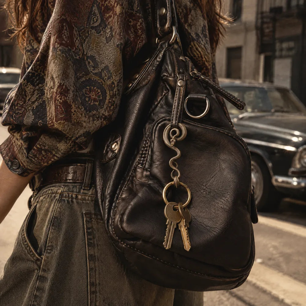 Coiled serpent keychain hanging on a leather bag with keys
