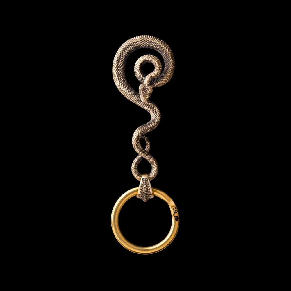 Coiled serpent keychain on its own in antiqued brass with black zircon eyes and hand-carved scales; the same design is also made to order in other materials.
