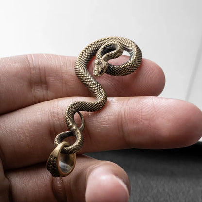 Close-up of the brass coiled serpent pendant held between fingers showing hand-carved scales; appearance reference for made-to-order editions