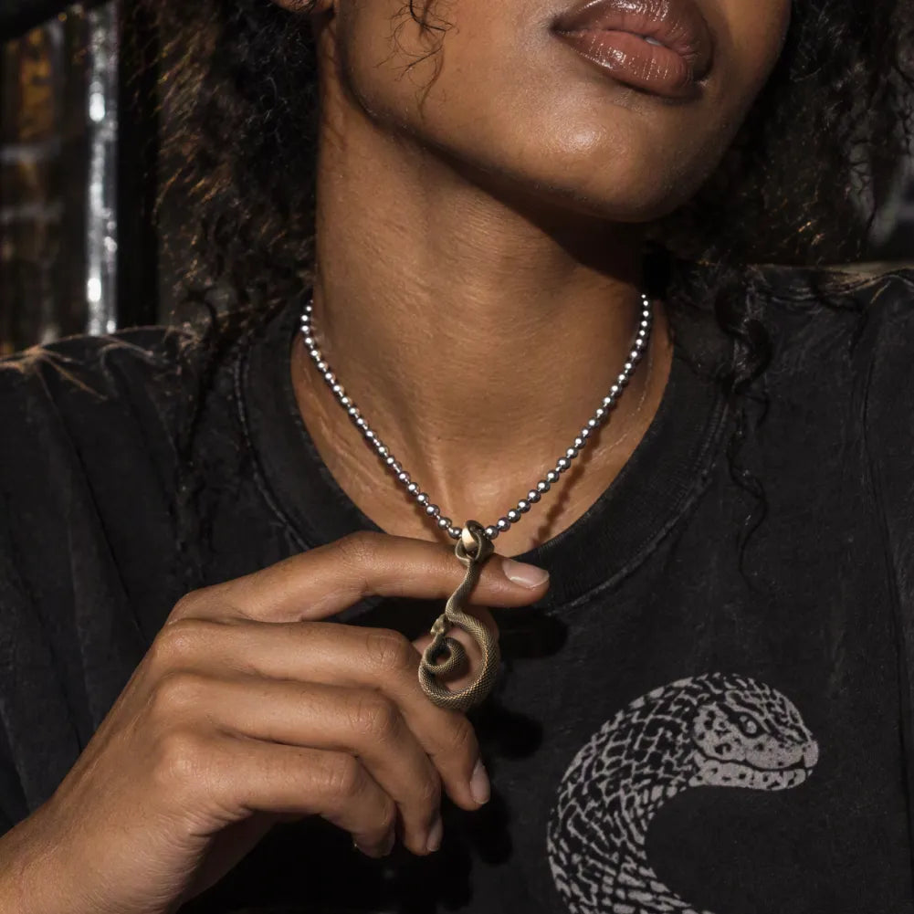 Woman holding her coiled serpent pendant over a black tee