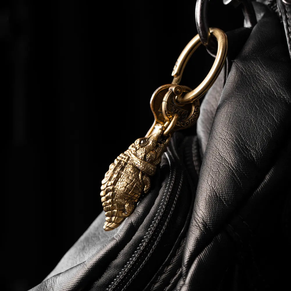 Crocodile pendant hanging from dark bag hardware.