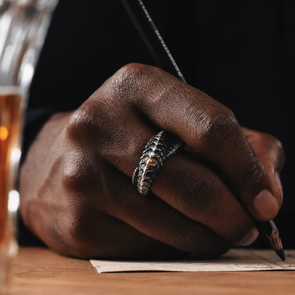 Dragon Scale Ring 2.0 worn on a man's hand beside a notebook