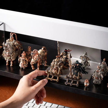A hand placing a bronze weapon rack among the Huang Zhong figure and other magnetic generals on a lit desk shelf
