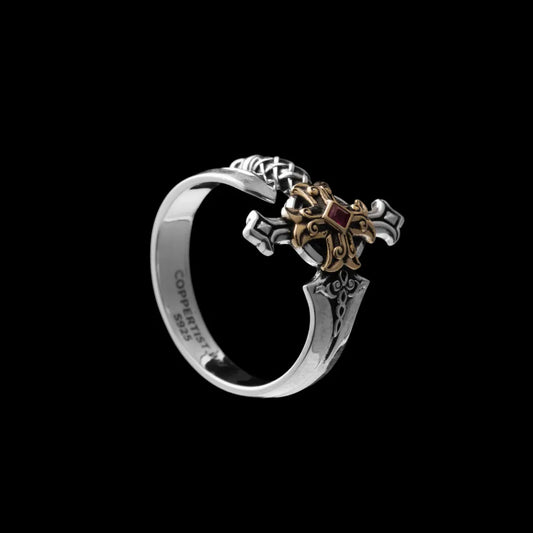 Judicator Blade ring with a silver-tone band, brass-tone sword details and a red center stone on a black background.