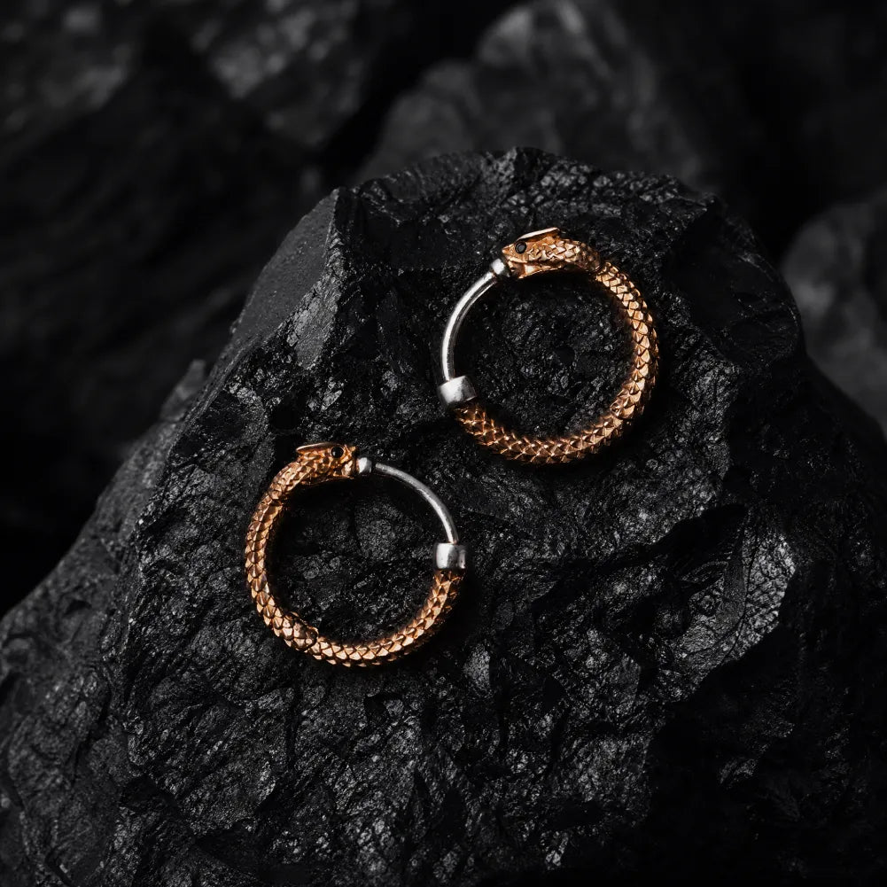 Pair of Ouroboros hoop earrings displayed on black stone