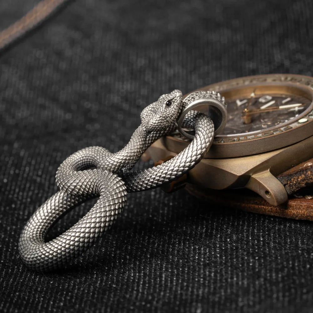 Snake Keychain in White Bronze, shown beside a wristwatch in a product close-up.
