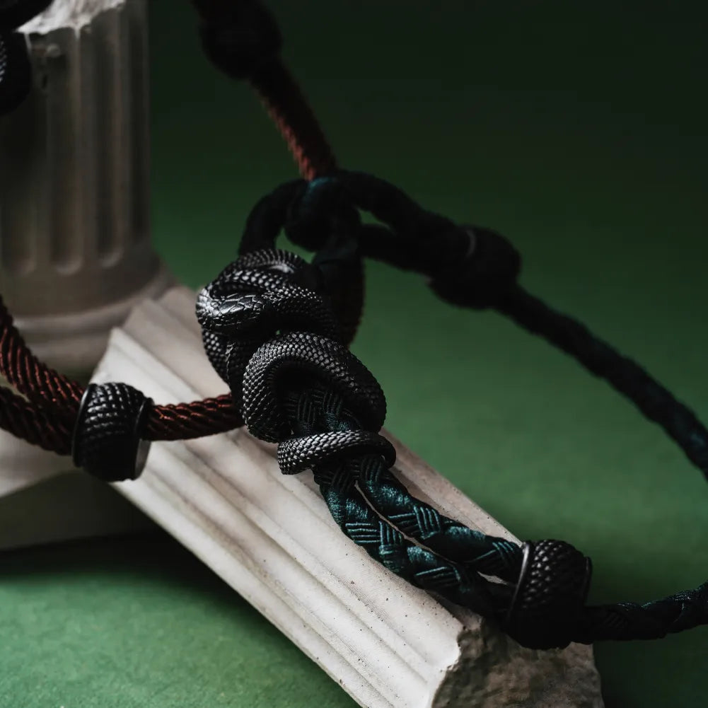 Blackened Tree Boa rope bracelet displayed on a green sculpture